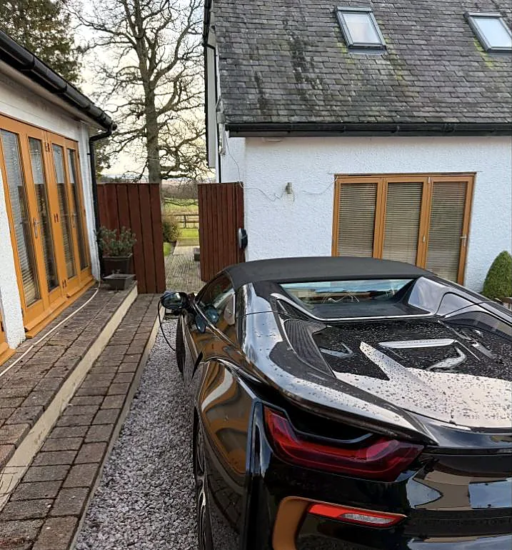 Electric car plugged in and charging on a driveway from a wall-mounted EV charge point installed by MMM Electrical near Glasgow