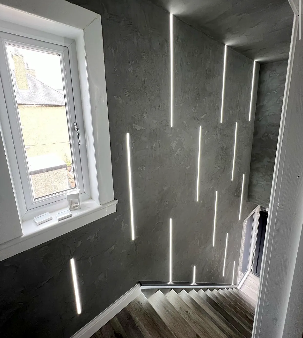 Recessed linear LED strips set into dark microcement walls and ceiling above a staircase