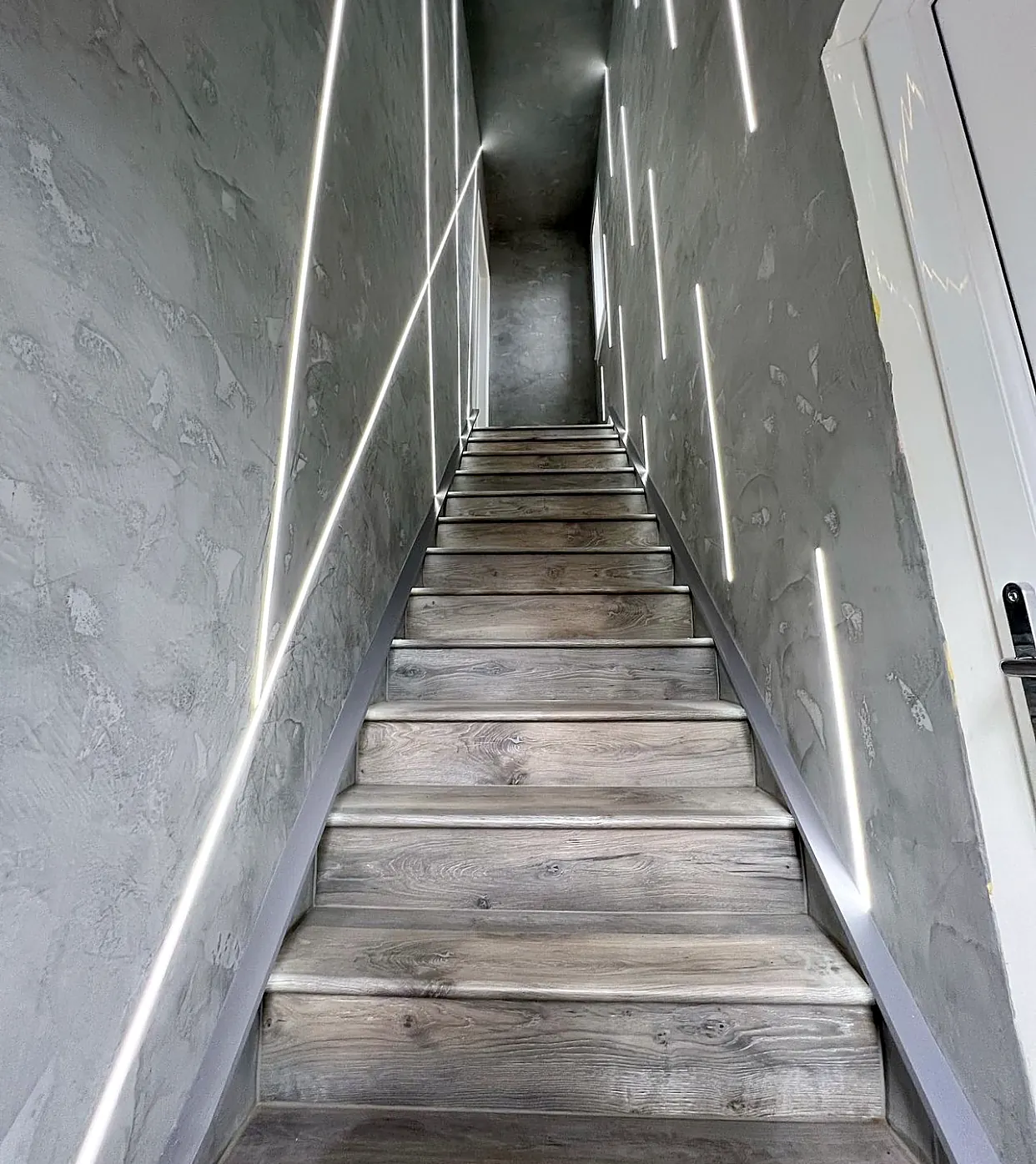 Staircase lit by recessed linear lighting on the surrounding walls