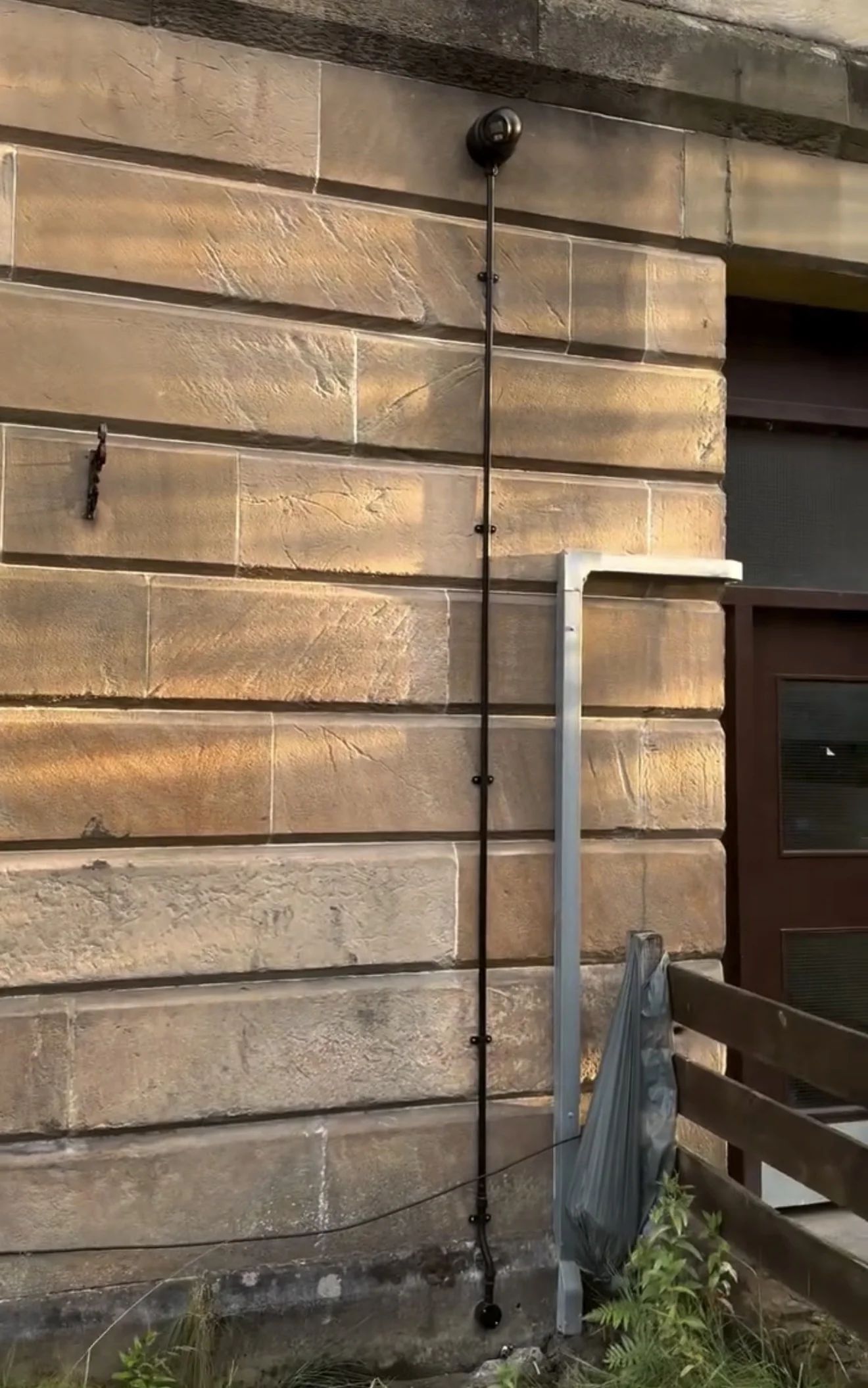 CCTV dome camera installed under the eaves of a sandstone building in Glasgow by MMM Electrical, with the camera cable run in surface conduit down the elevation