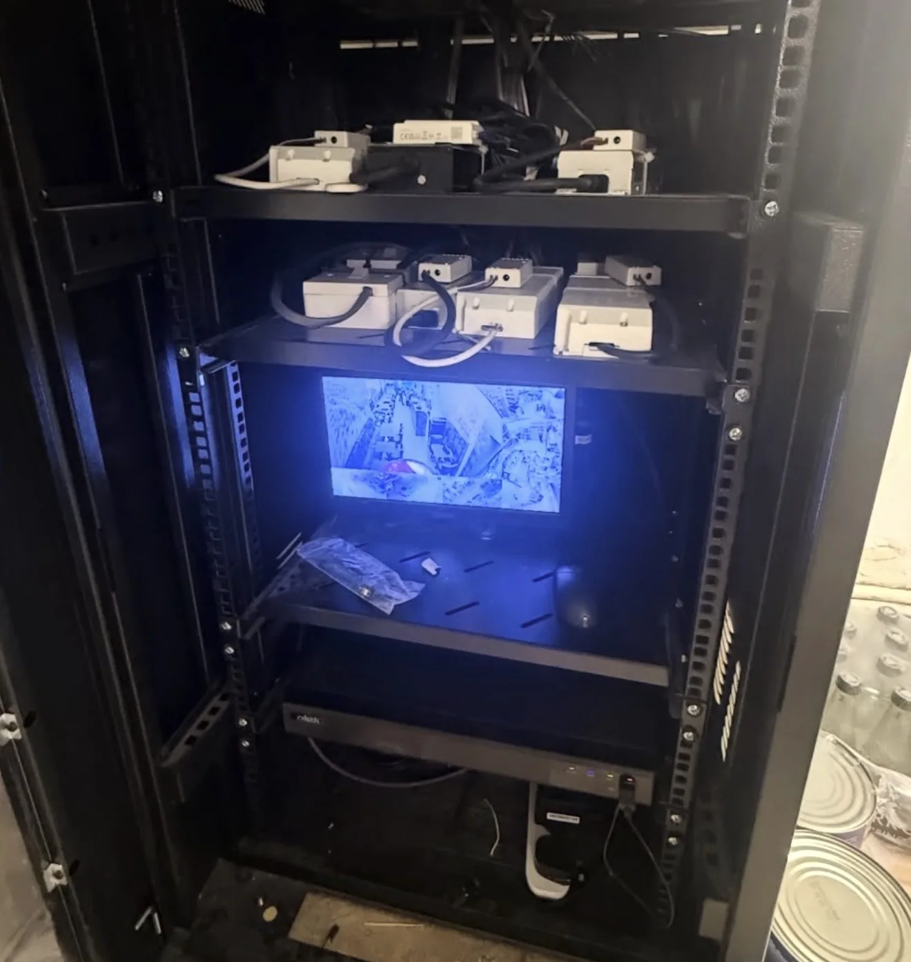 CCTV recorder and monitor installed in a comms rack by MMM Electrical, showing a live multi-camera view alongside power supplies
