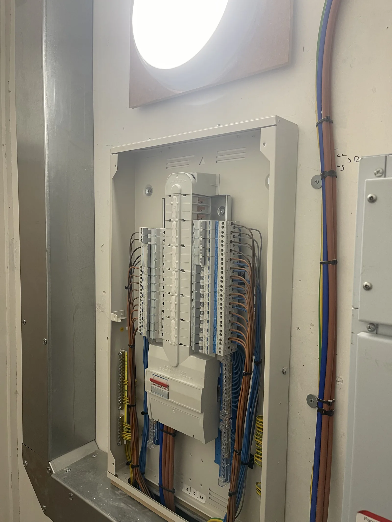 Three-phase distribution board installed in a commercial plant room by MMM Electrical, with containment and a bulkhead light above