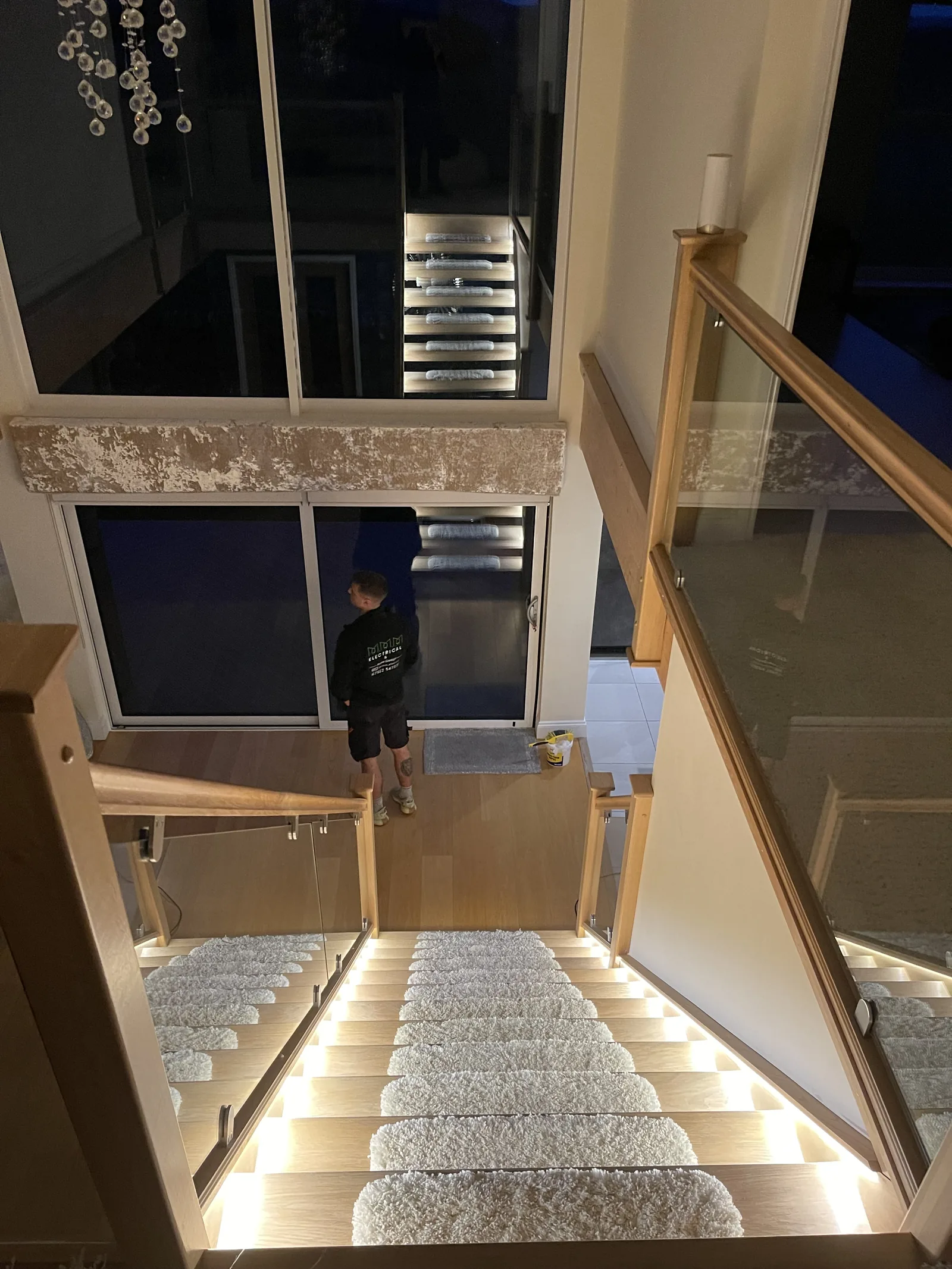 Oak staircase with a glass balustrade lit by concealed LED strips installed under each tread by MMM Electrical